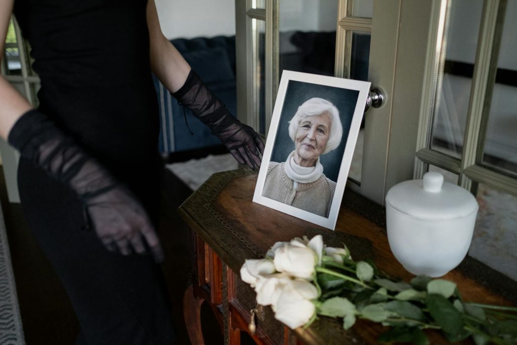 A reflective moment at a memorial with a framed portrait of an elderly woman, flowers, and an urn.