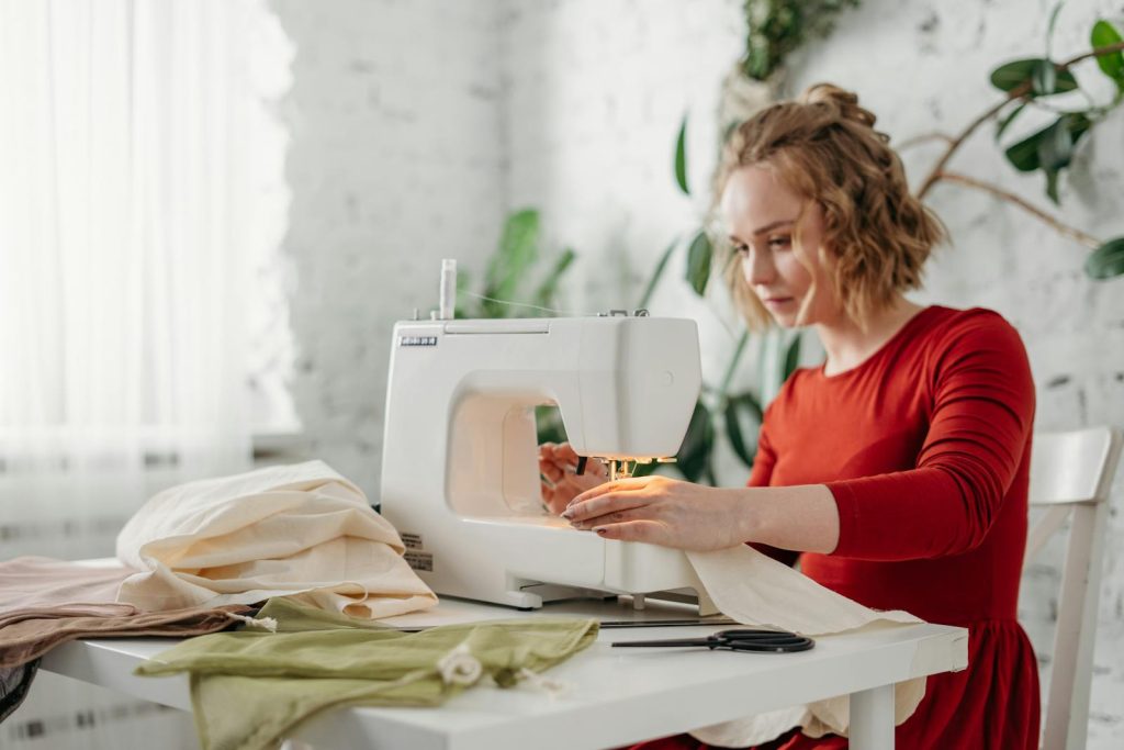 A woman in a red dress using a sewing machine at home, creating a handmade garment. skredderpriser, skredder, priser