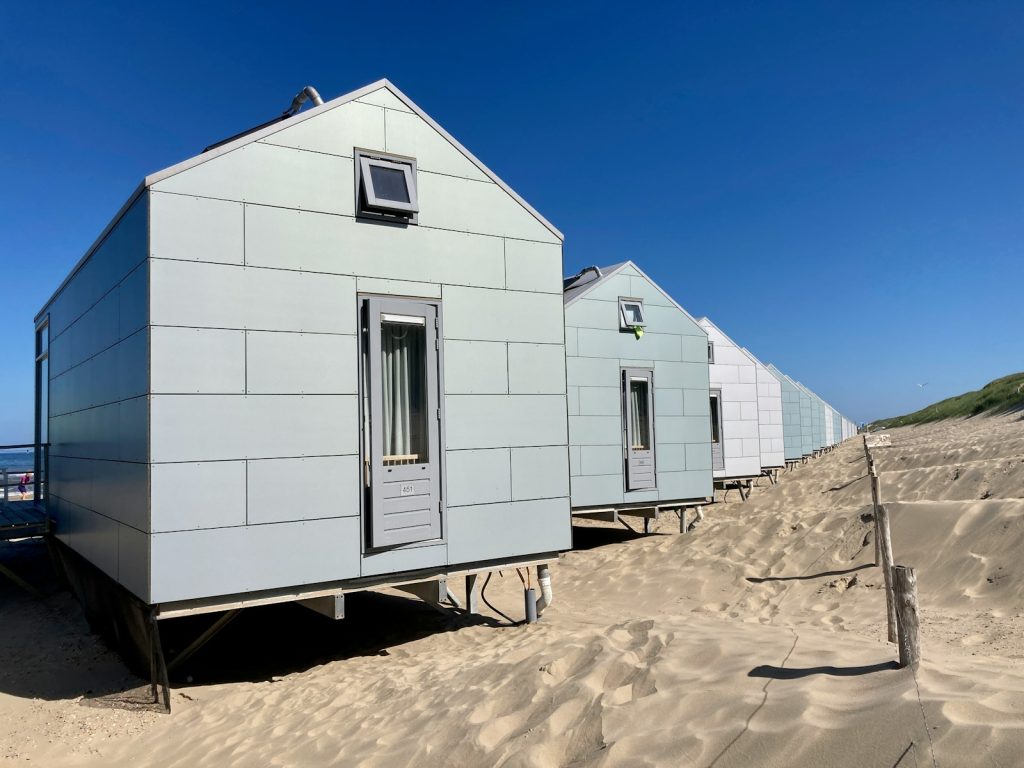 white concrete house on brown sand under blue sky during daytime, leie hytte, airbnb, priser, hytte ved sjøen