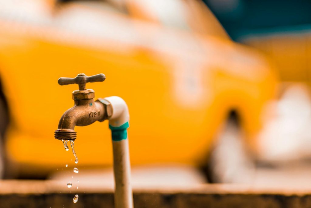 Macro shot of a brass faucet with water droplets against a blurred yellow background. vannlekasje, rørlegger